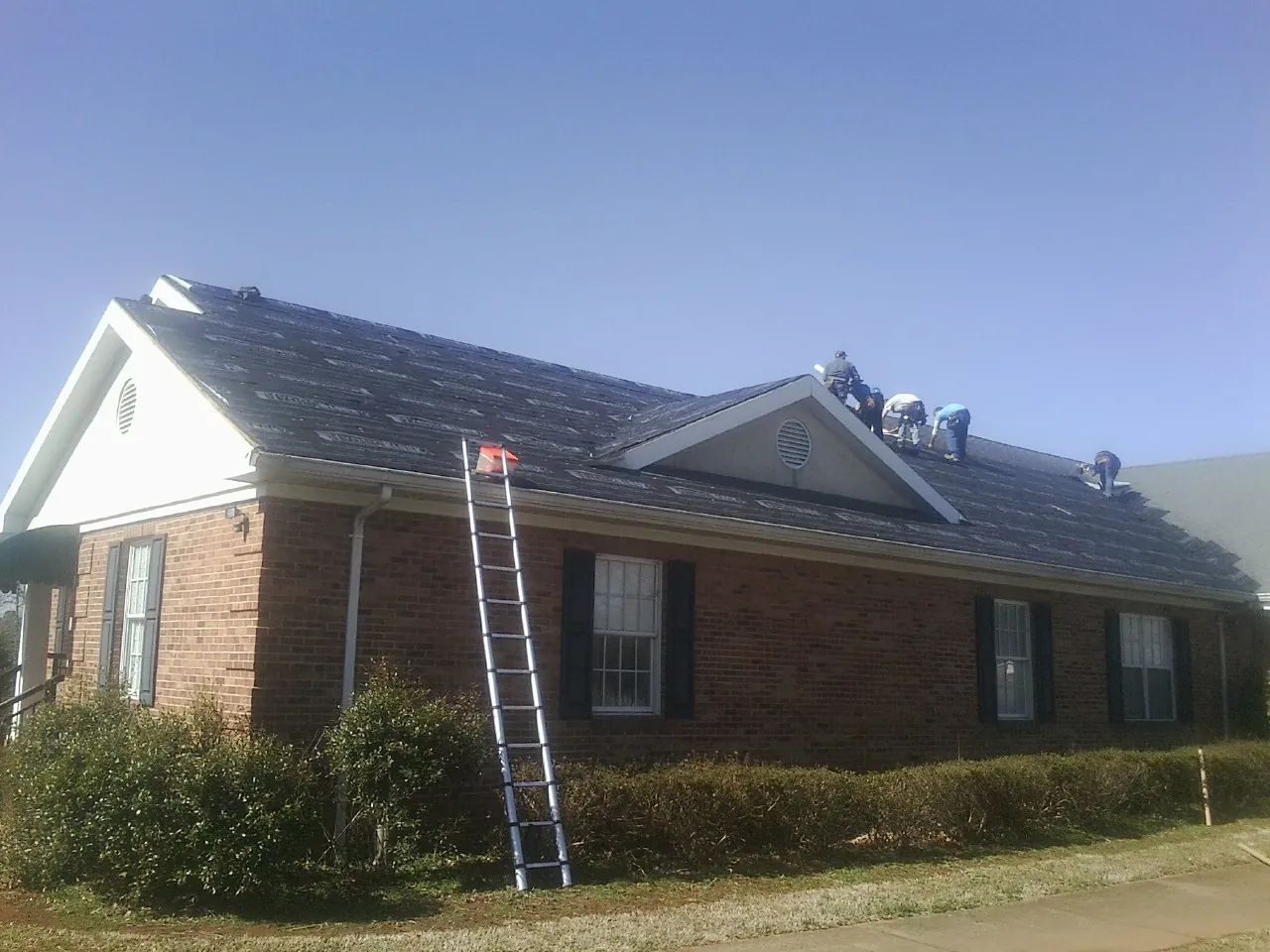 Crew tearing shingles off a brick ranch roof with a ladder set — Emergency Roof Repair work by our crew in Hawthorne