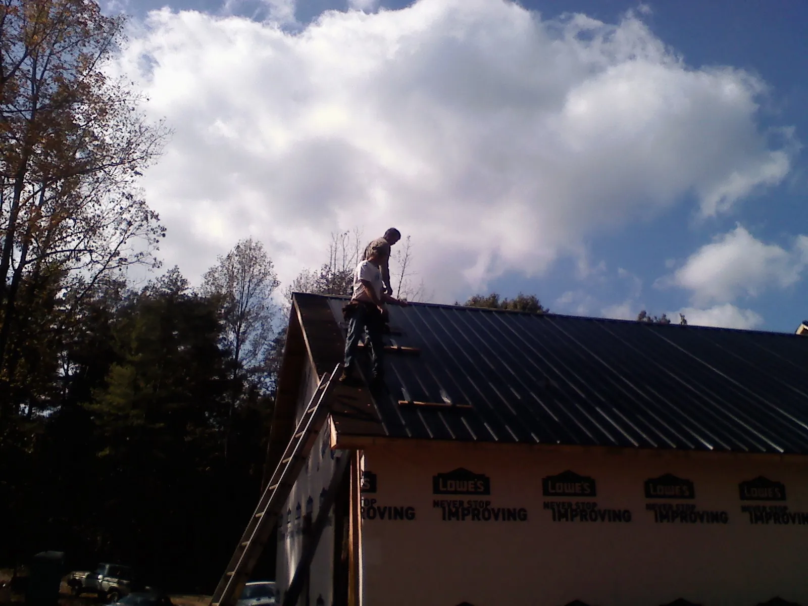 Roofer fastening dark metal panels high against a cloudy sky, from a Roof Inspection job in Hawthorne