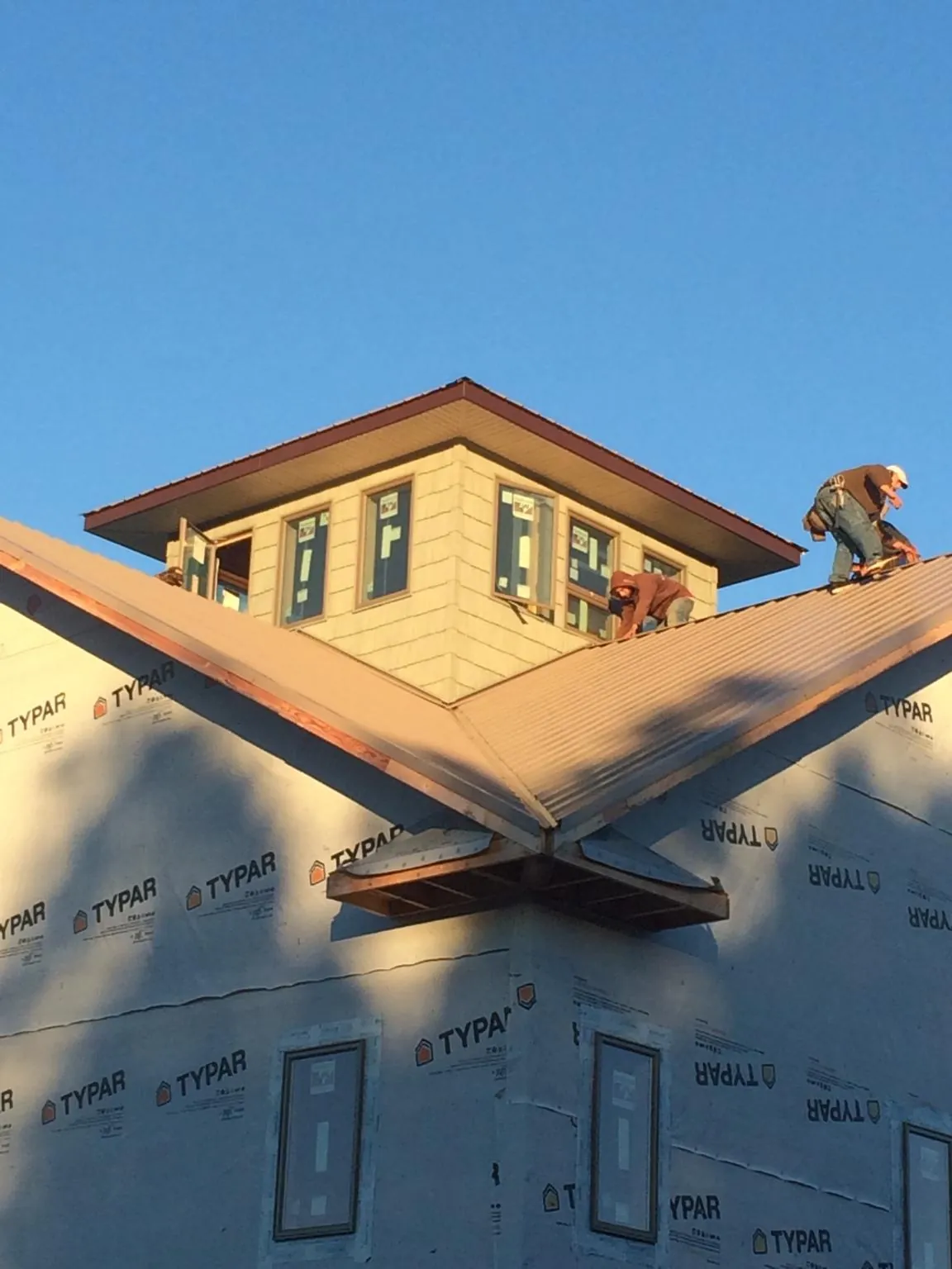 Roofers working around a rooftop cupola on a new metal roof at sunset in Hawthorne